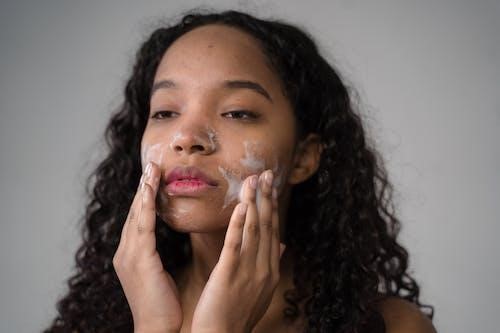 African American female with long dark curly hair washing cheeks with facial foam
