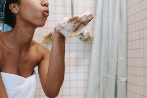 African American woman in bath using antidandruff shampoo, blowing bubbles