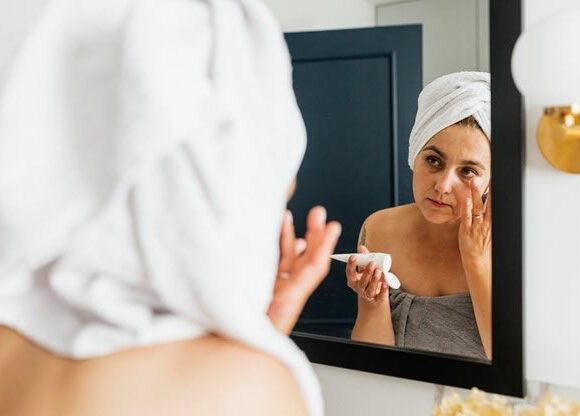 The Best Antifungal Creams for Face - Woman Looking in mirror -using Anti fungal cream on her face