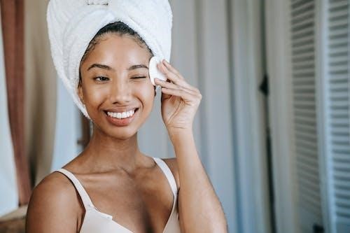 Smiling ethnic woman wiping face skin during morning cleanse